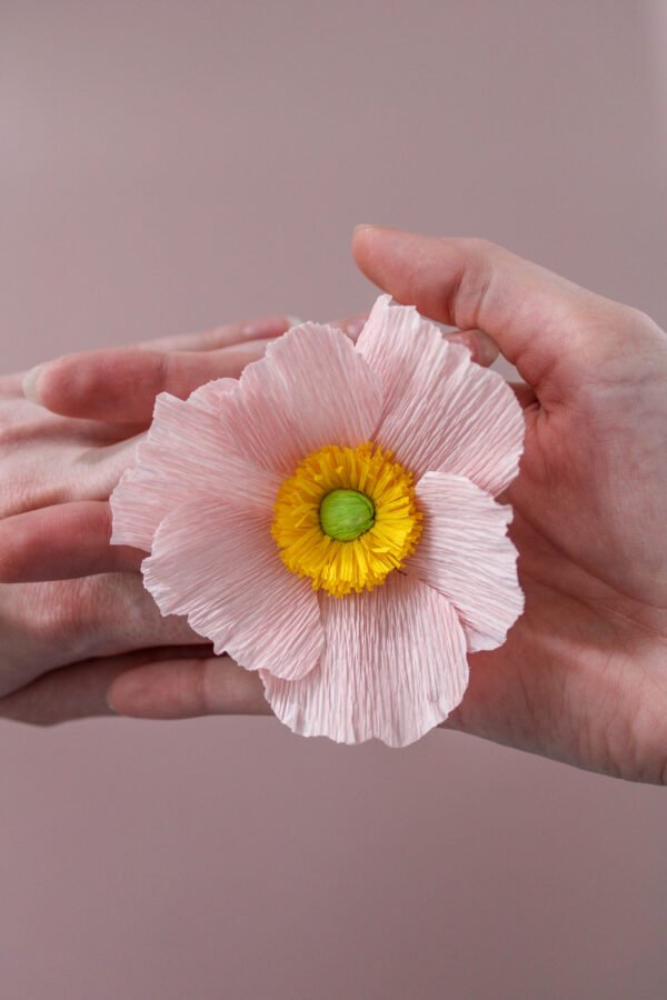 Anémone de Japon en papier positionnée sur deux mains entrelacées.